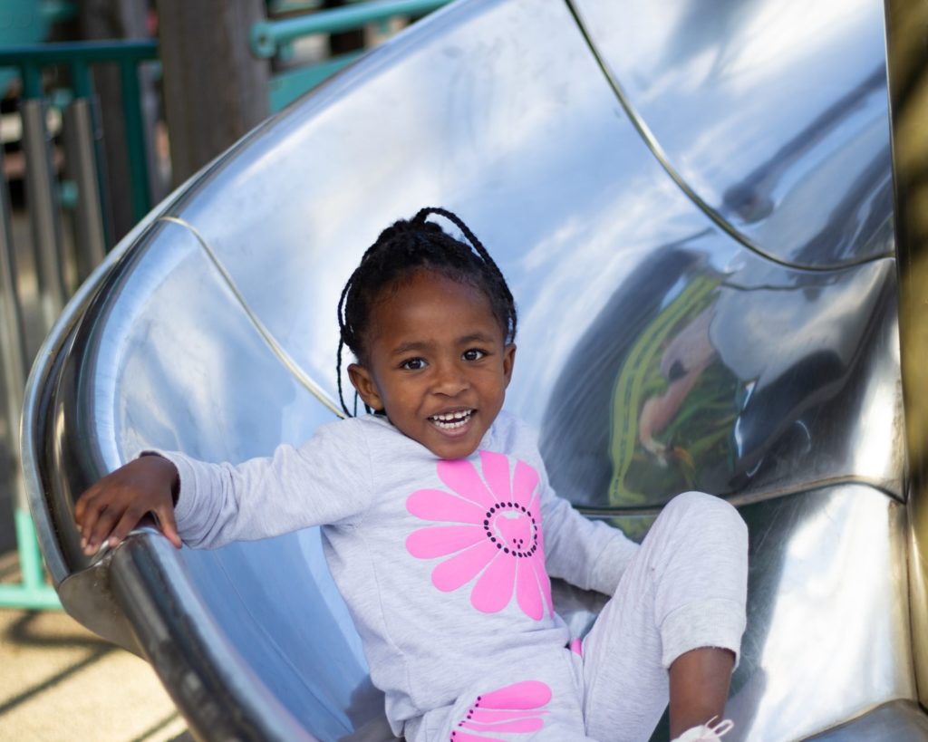 Child smiling at the end of a playground slide